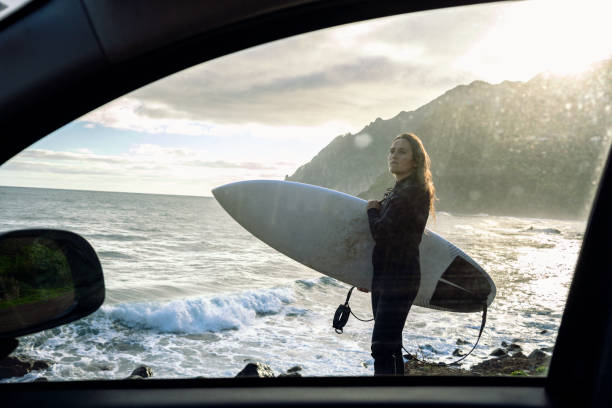 Surfer girl getting away from it all. Middle aged woman near her car with her surfboard at sunset.