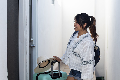 Portrait of a woman traveling alone, smiling standing at the door of her accommodation in Mexico with her luggage, suitcase and backpack next to her