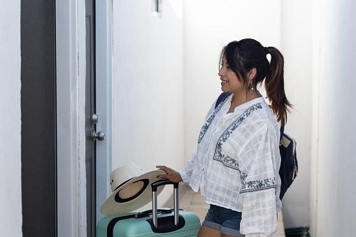 Woman smiling on her solo trip, standing at the door of her room in Mexico with her luggage