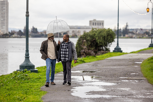 Same-sex couple of African American decent taking a brisk walk by a lake on a rainy day.