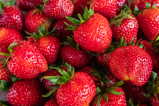 Close-up view of fresh red organic strawberry background with green leaves, sweet fruit that provides vitamins.