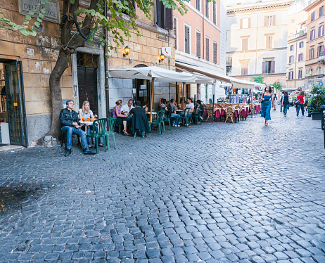 Rome Italy - May 22 2011; Woman in blue walks towards past sidewalk cafe patrons in city cobblestone street.