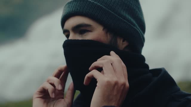 Face of young man adjusting neck warmer in Iceland. Slow motion