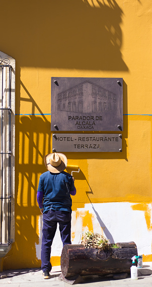 Oaxaca, Mexico: A man painting a vibrant yellow wall of a hotel-restaurant in downtown Oaxaca.