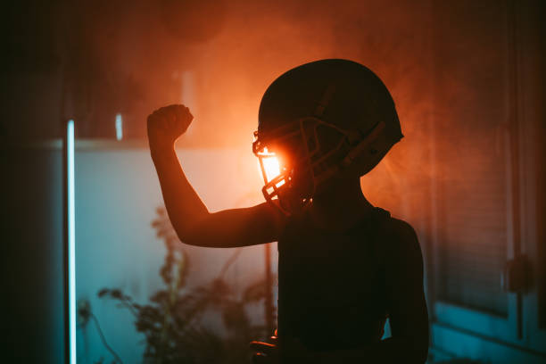 Side view of boy wearing American football helmet showing biceps under colorful neon lights at home in the evening
