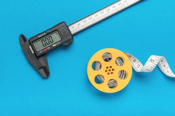 An electronic vernier caliper and a coil with a measuring tape on a blue background. A tool for accurate measurement of dimensions.