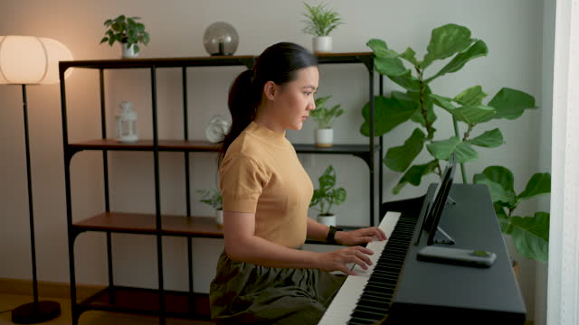 Asian woman using tablet for remotely learns online to play the piano at home.