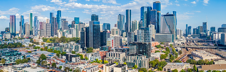 Aerial wide angle panoramic view Melbourne CBD with impressive clusters of high-rise buildings and architecture, varied eras of North Melbourne buildings and architecture, tree-lined streets in foreground.   Southern Cross Railway Station and railway maintenance facility is on the far right hand side of the panoramic view. Multiple logos, none dominant, stitched panorama.