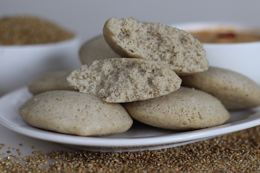 Bajra idly. Steamed savory rice cake made by a batter of fermented de husked black lentils and unpolished pearl millet. Shot on white background along with bajra on the background