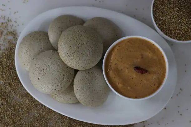 Photo of Bajra idly served with spicy coconut condiment. Steamed savory rice cake made by a batter of fermented de husked black lentils and unpolished pearl millet