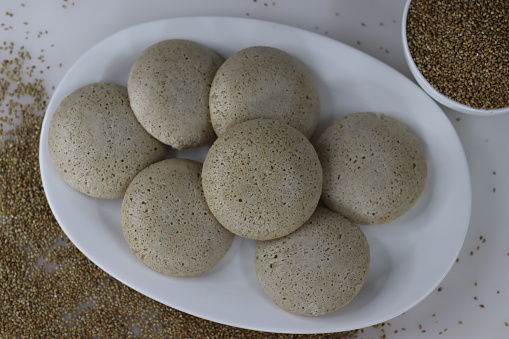 Bajra idly. Steamed savory rice cake made by a batter of fermented de husked black lentils and unpolished pearl millet. Shot on white background along with bajra on the background