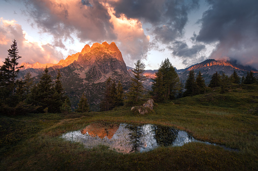 Summer landscape view of a mountain range illuminated at sunrise and reflecting into a pond with dark clouds