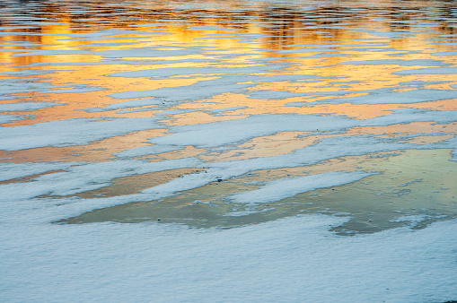 The golden sunset is reflected on the icy lake, creating warm hues and a calm atmosphere.