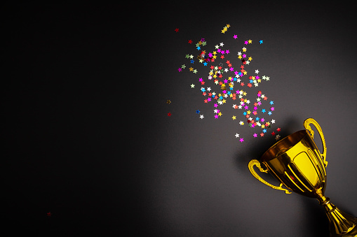 Cup trophy on black background, confetti celebration, first-place win, victorious competition