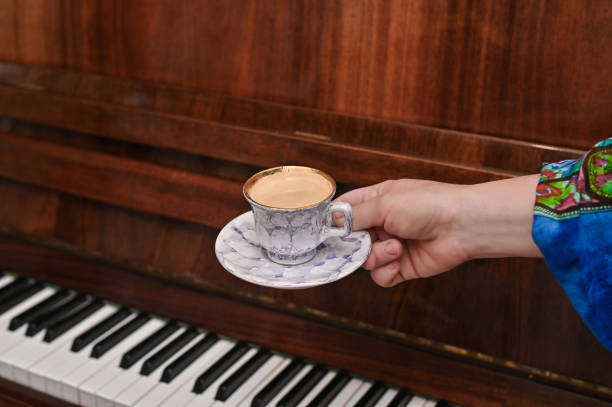 koncepcja muzycznej pauzy podczas lekcji muzyki. filiżanka kawy w dłoni na tle starego pianina. - music coffee espresso theatrical performance zdjęcia i obrazy z banku zdjęć