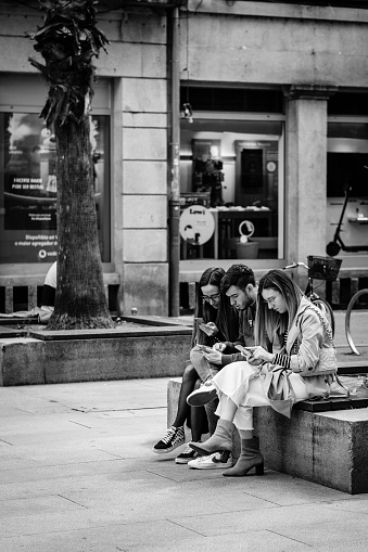Pontevedra, Spain - March 26, 2022: A group of young people look at their smartphones sitting in the historic center of the village.