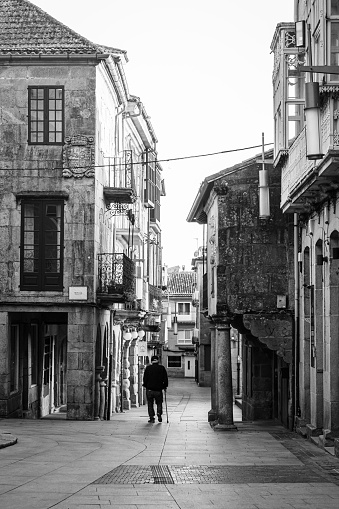 Pontevedra, Spain - July 7, 2022: An old man using a cane, walks through one of the streets of the historic center of the city.
