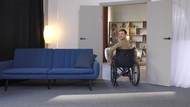 A handsome young man in a wheelchair moves around the apartment, getting used to a new life. Recovery after injury or ill lonely at home