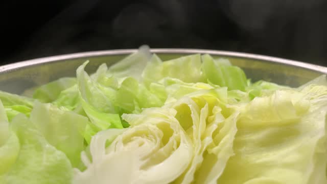 Hot steaming fresh market sweetheart cabbage rotating as it is being steamed in a stainless steel steamer pot.