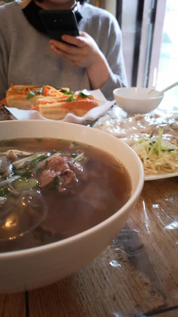 Closeup vertical shot of Pho soup, Banh mi and Banh cuon on a table in a restaurant