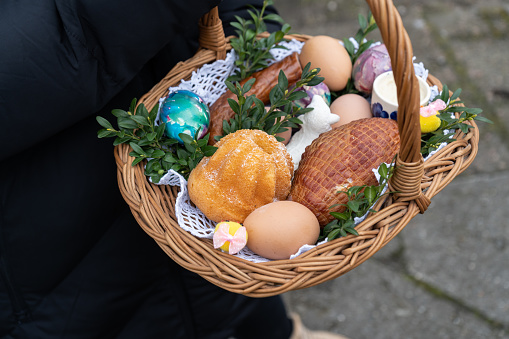 Woman holding Easter basket for blessing in a church. Traditional woven wicker Paschal basket filled with various food, ready to be blessed by a priest as part of the Easter tradition.