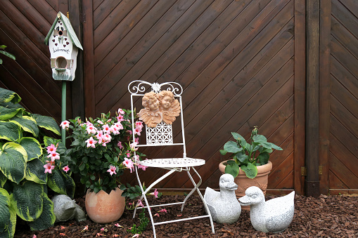 Nostalgic garden design with flowers, old chair and stone figures.