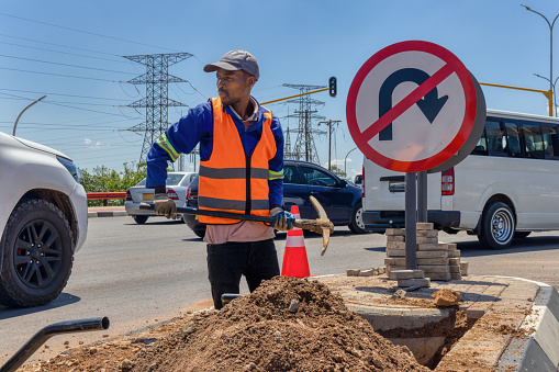 african american worker with a pickaxe digging a ditch in the highway to repair cabling on an isle at an intersection