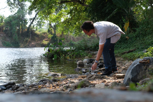 istock Young Asian man bending himself to keep plastic bottle from river to keep clean in nature, natural water source with freshness of green tree background. 2019688110