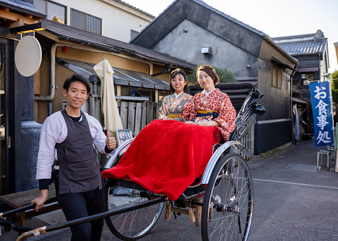 Portrait of female tourists in Kimono / Hakama with a rickshaw driver in traditional Japanese town