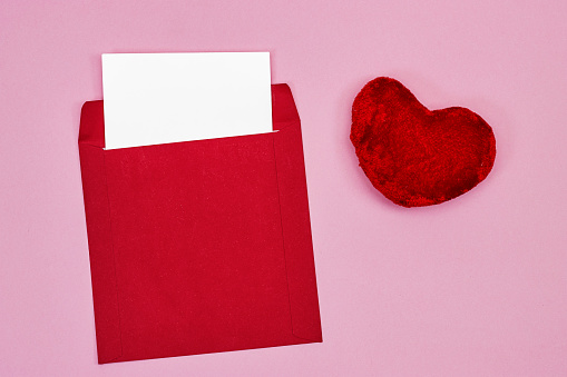 Wedding invitation card mockup and red envelope with red heart toy on pink background. Blank card mockup