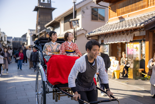 Female tourists in Kimono / Hakama riding ‘Jinkirisha’ rickshaw in traditional Japanese town