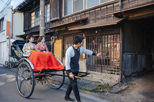 Female tourists in Kimono / Hakama riding ‘Jinkirisha’ rickshaw in traditional Japanese town