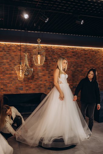 Bride at the clothes shop for wedding dresses she is choosing a dress and the designer are assisting her. High quality photo