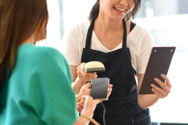a female customer and a young asian female clerk making cashless mobile payment at a restaurant - soda jerk 뉴스 사진 이미지