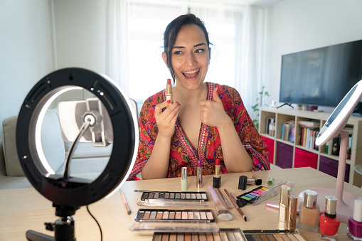 Beauty blogging, technology and people concept portrait of a happy smiling woman blogger with ring light and smartphone applying make up at home.making a influencer video