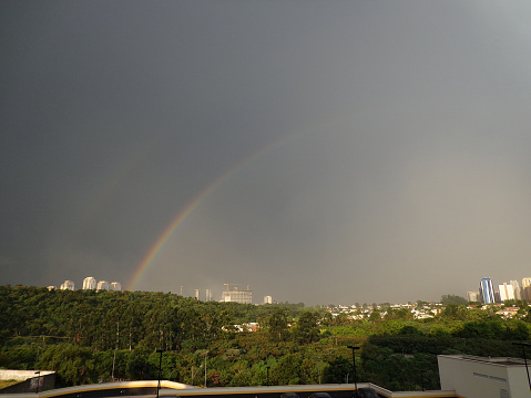 A bright large and dense rainbow in a gray cloudy sky above city houses after the last thunderstorm, image with copy space.