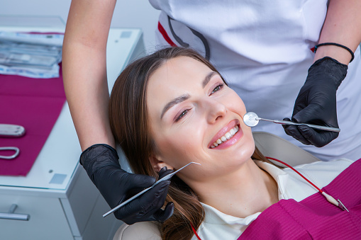 Beautiful woman with healthy straight white teeth sitting at dental chair with open mouth during a dental procedure. Dental clinic. Stomatology