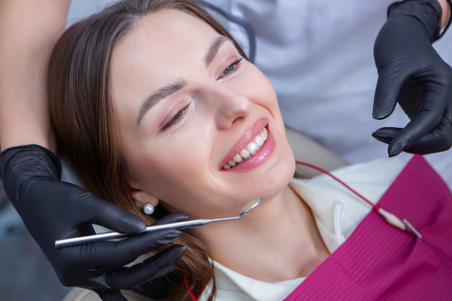 Beautiful woman with healthy straight white teeth sitting at dental chair with open mouth during a dental procedure. Dental clinic. Stomatology