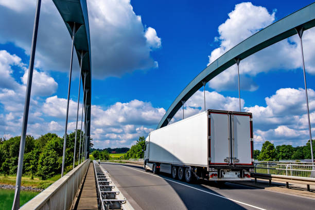 White truck driving down highway bridge over river stock photo