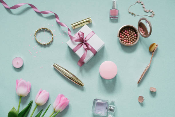 ピンクの花、チューリップ、化粧品、弓付きのギフトボックスを備えた女性ブロガーのデスクトップ。フラットレイ