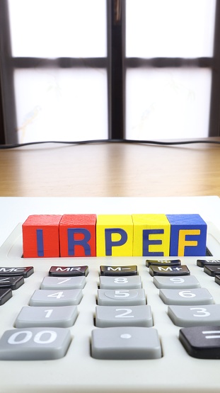 Written IRPEF in Italian is the tax payable by natural persons. Written on wooden cubes. Calculator and window background.