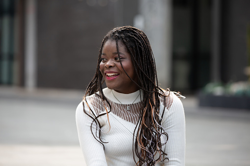 Portrait of beautiful young African American woman showing long black hair braided hairstyle while feeling happy and smiling in the city outdoor