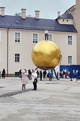 Salzburg, Austria - December 23, 2023: Golden sphere with a man - sculptor Stephan Balkenhol on Kapitelplatz square. Unidentified people are walking on the square