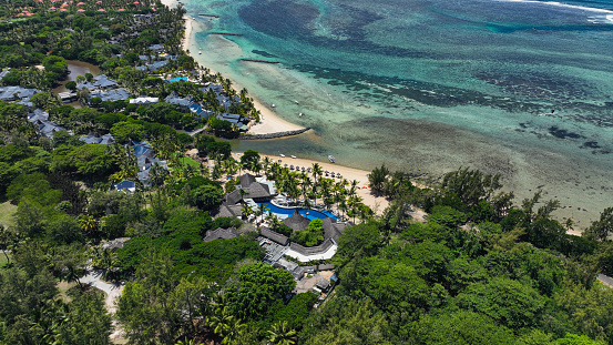 An overhead view of a resort situated on a scenic beach in Mauritius, showcasing its facilities, pool, and surrounding tropical landscape.
