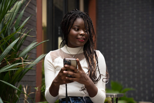 portrait of beautiful young african american woman showing long black hair braided hairstyle and using mobile phone while feeling happy and smiling in the city outdoor - braided braids women long hair imagens e fotografias de stock