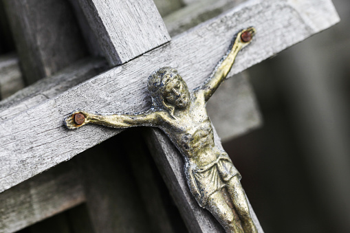 Act of vandalism. Broken stone cross. Metal rusty Jesus figure.