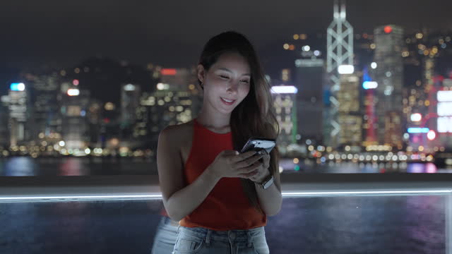 A woman using holding a smartphone against city night view in Hong Kong