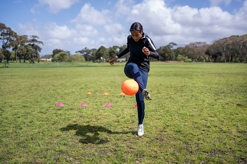 Young female soccer player juggling a soccer ball on sports field during training session