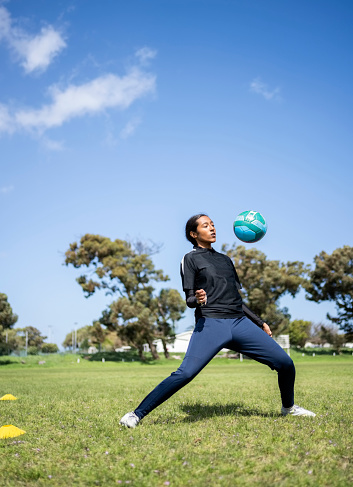 Young girl soccer player juggling a soccer ball on sports field during training session