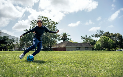 Focused young female footballer in sports clothing practicing dribbling in sports training drill on ground